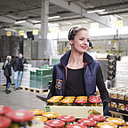 ALDI SÜD Auszubildene hebt eine Palette Gläser in der Logistikhalle hoch und schaut zur Seite
