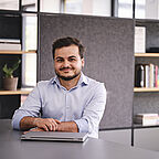 ALDI SÜD Auszubildener sitzt mit einem Laptop vor sich am Schreibtisch im Büro und lächelt in die Kamera