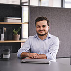 ALDI SD Auszubildener sitzt mit einem Laptop vor sich am Schreibtisch im Büro und lächelt in die Kamera