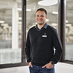 ALDI SÜD Mitarbeiter steht vor den Bürofenstern der Logistik und lächelt freundlich in die Kamera