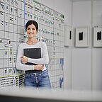 ALDI SÜD Mitarbeiterin lehnt sich im Büro der Logistik an die Tourentafel und lächelt in die Kamera