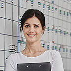 ALDI SÜD Mitarbeiterin steht vor der Tourentafel im Büro der Logistik und lächelt in die Kamera