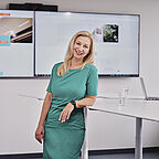 ALDI SÜD Mitarbeiterin der Verwaltung lehnt sich an einen Schreibtisch und lächelt in die Kamera